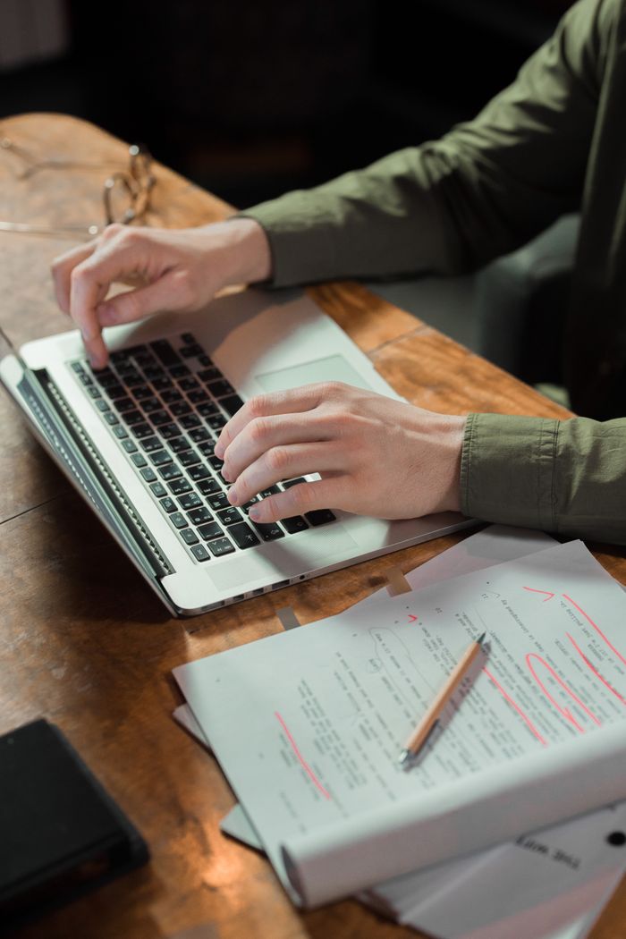 Mastering the First Impression: Your intriguing post title goes here Focused person typing on laptop with notes and papers beside on wooden table.